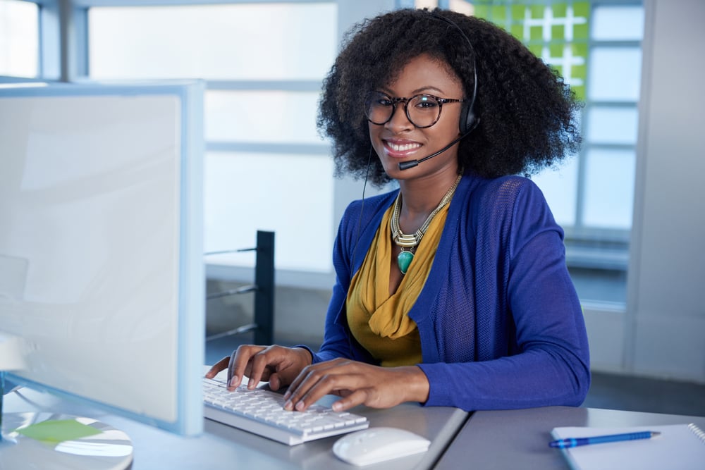 Portrait of a smiling customer service representative with an afro at the computer using headset Portrait of a smiling customer service representative with an afro at the computer using headset